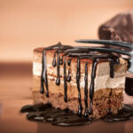 Chocolate dessert slice with layered mousse and dripping chocolate sauce, featured in a post about hobbies related to food and cooking.