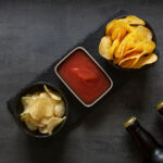 Chips and salsa served in black bowls on a dark slate tray, with a bottle of soda in the corner, highlighting snack options for casual gatherings.